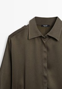 Chemise olive verte à boutons avec col, ornée d'épaulettes et en tissu lisse et texturé. L'étiquette indique "Massimo Dutti."