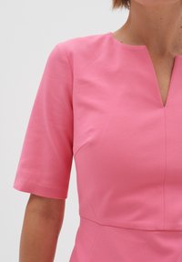 Rosa klänning med åtsittande överdel, korta ärmar och V-ringning. Slät tygkvalitet och strukturerade sömmar. Enkelt, enfärgat design.