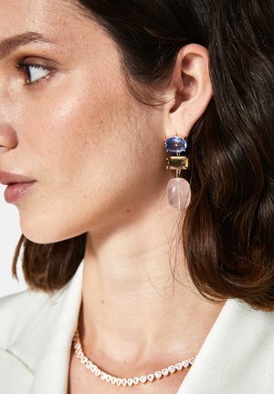 Ohrringe aus Gold und blauen Edelsteinen, die ein geschichtetes Design mit einem runden pinken Akzent aufweisen. Der Gesamteindruck ist facettenreich und durchsichtig.