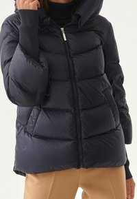 Sininen pehmeä takki hupulla, jossa on etuvetoketju, ribbikujat ja tikattu muotoilu. Sujuva, kiiltävä kangas ja rento malli.