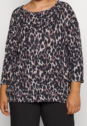 Vrouw draagt een langarmige top met luipaardprint met zwarte, bruine en beige vlekken, gecombineerd met effen zwarte broek.
