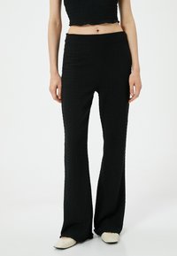 Zwarte flared broek met een gestructureerde stof, voorzien van een hoge taille, elastische band en gladde naden. Draag het met beige schoenen.