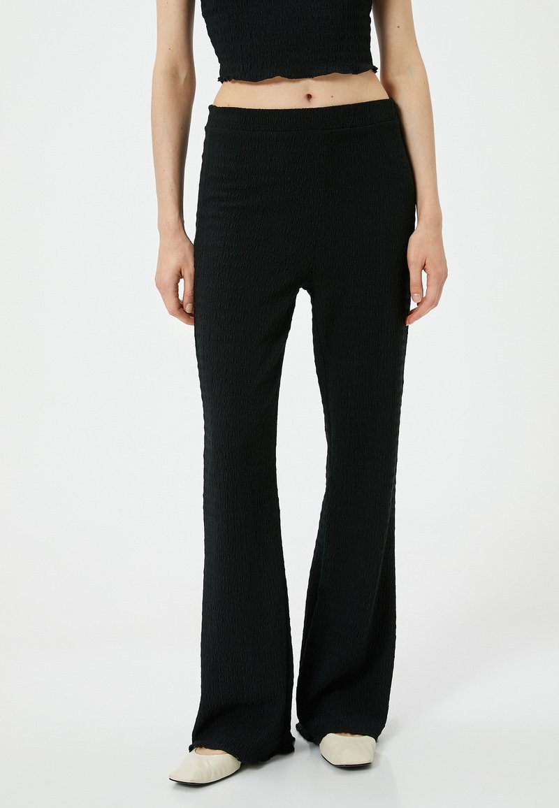 Zwarte flared broek met een gestructureerde stof, voorzien van een hoge taille, elastische band en gladde naden. Draag het met beige schoenen.