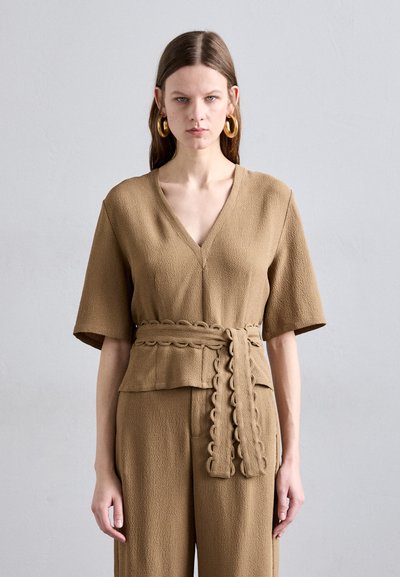 Tan textured top with a V-neck and short sleeves, featuring a matching belt with a scalloped design, paired with wide-leg trousers.