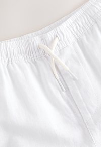 Close-up of white fabric shorts with an elastic waistband and tied white drawstring at the center front.