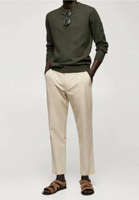 Dunkelgrüner gestrickter Pullover, cremefarbene gestreifte Hose und braune Sandalen mit Riemen. Das Outfit hat eine lockere Passform und leichte Texturen.