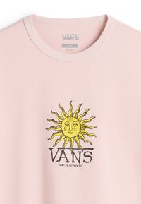 Světle růžové bavlněné tričko s kulatým výstřihem. Uprostřed se nachází žlutý grafický motiv slunce nad logem "VANS" a textem "Always Authentic".