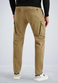 Pantalons cargo kaki avec plusieurs poches latérales, coupe droite et en matériau coton. Stylés avec des baskets blanches.