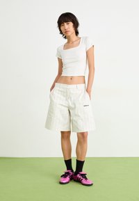 Vit, kortärmad crop top och beige randiga shorts med fickor. Svarta strumpor med rosa skor, med svarta detaljer och kardborreband.