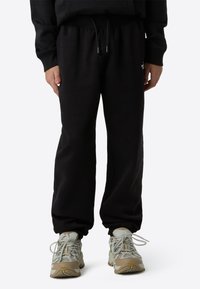 Svarte joggebukser laget av mykt stoff, med elastisk midjebånd og snøring, samt innsnevrede mansjetter ved ankler.