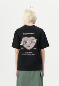 Black cotton t-shirt featuring a large heart graphic with "Carhartt WP" and text in white and pink. Round neckline and short sleeves.