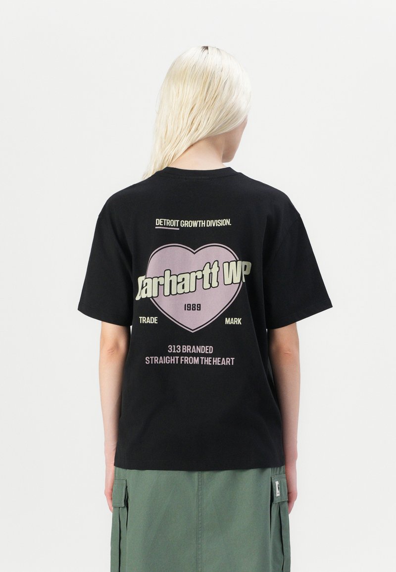 Black cotton t-shirt featuring a large heart graphic with "Carhartt WP" and text in white and pink. Round neckline and short sleeves.