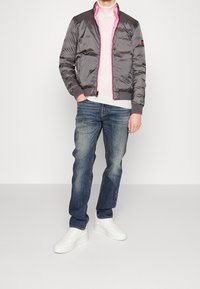 Šedá vycpaná bomber bunda s růžovým interiérem, vroubkovanými manžetami a kapsami na zip, v kombinaci s modrými džíny a bílými teniskami.