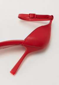Sandale à talons hauts rouges avec un dessus en cuir élégant, une fine bride de cheville et un design à bout pointu. Le talon transparent ajoute une touche moderne.