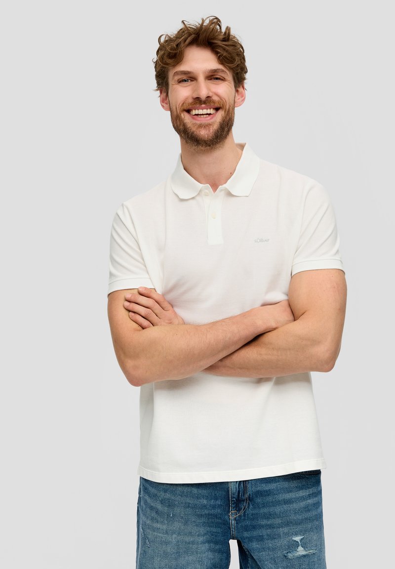 Weißes Polohemd aus strukturiertem Stoff, mit kurzen Ärmeln und klassischem Kragen. Auffällige Details sind zwei Knöpfe am Ausschnitt.