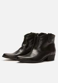 Botas de cuero negro hasta el tobillo con punta afilada, cremalleras en los laterales, detalles en relieve en la parte frontal y un tacón bajo apilado.