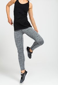 Sort tanktop, grå teksturerede leggings med slank pasform og kontrastsyninger, parret med sorte atletik sko med hvide detaljer.
