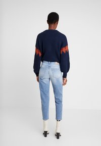 Námořnicky modrý pletený svetr s oranžovým cik-cak vzorem na rukávech, spárovaný se světlými modrými džíny. Modelka nosí krémové kotníkové boty s masivním podpatkem.