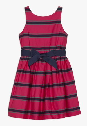 Robe rouge sans manches avec des rayures horizontales noires et vertes, jupe plissée, et nœud bleu marine à la taille.
