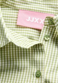 Roheline ja valge ruuduline särk roheliste nööpidega ning roosakas sildiga, millel on krae sees brändinimi JJXX.