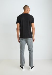 Camiseta de algodón negra con cuello redondo clásico, combinada con jeans de mezclilla grises. Los zapatos presentan un diseño en blanco y negro, con una suela gruesa.