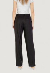 Pantaloni neri a gamba larga con una texture liscia, caratterizzati da una vita e una singola tasca posteriore, abbinati a un top bianco aderente.