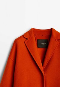 Cappotto in lana rosso-arancio con rever a vista, chiusura a un bottone e finitura testurizzata. Presenta un'etichetta interna nera.