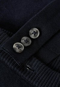 Maglione lavorato a maglia blu navy con polsini a coste, tre bottoni trasparenti, tessuto texturizzato e un piccolo'apertura per il fissaggio dei bottoni.