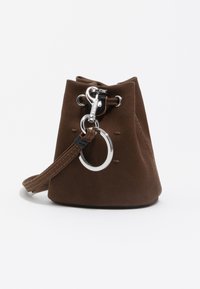 Bolso tipo bucket de ante marrón con cierre de cordón, herrajes plateados y una correa para la muñeca. Destaca un anillo decorativo en la parte frontal.