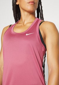 Nike ärmlöst atletiskt linne i en rosafärgad nyans med rundad halsringning och svarta axelband. Har en liten vit logotyp på bröstet.
