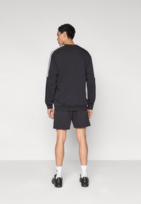 Μαύρο φούτερ με λευκές ρίγες στους ώμους, συνδυασμένο με μαύρο σορτς. Το σύνολο έχει άνετη εφαρμογή και είναι κατασκευασμένο από μαλακό ύφασμα.