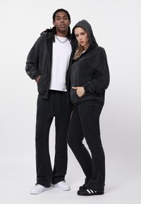 Μαύρα φούτερ και παντελόνια από μαλακό υλικό, που ταιριάζουν μεταξύ τους, με κουκούλες και τσέπες. Τα αξεσουάρ περιλαμβάνουν μια αλυσίδα και παπούτσια σε αντίθετο χρώμα.