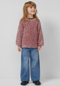 Sweter dziecięcy typu pulower w mieszance różowego i czerwonego, miękki w dotyku, z szerokimi rękawami, w zestawieniu z niebieskimi szerokimi dżinsami i czarnymi butami. Prosty, codzienny strój.