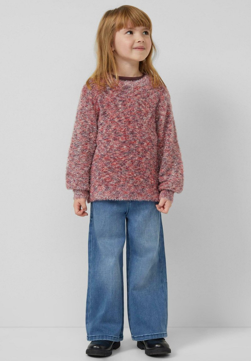 Sweter dziecięcy typu pulower w mieszance różowego i czerwonego, miękki w dotyku, z szerokimi rękawami, w zestawieniu z niebieskimi szerokimi dżinsami i czarnymi butami. Prosty, codzienny strój.