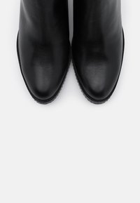 Schwarze Lederstiefeletten mit einer glatten, glänzenden Oberfläche, spitzen Zehen und einer gummierten Sohle mit niedrigem Profil. Keine sichtbaren Beschläge oder Verzierungen.