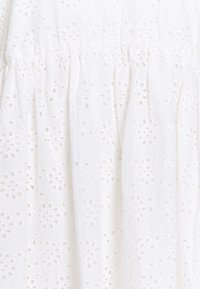 Wit katoenen jurk met een bloemig broderie anglaise ontwerp, voorzien van textuurpatronen en plissé-details bij de taille.