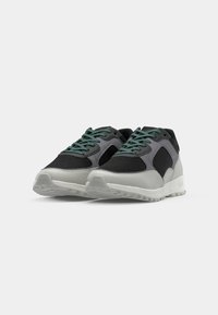 Black and gray sneakers with mesh panels, textured surfaces, green laces, and a white rubber sole featuring a tread pattern.