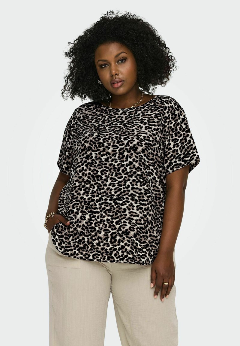 Haut à manches courtes en tissu doux avec un motif léopard, présentant une coupe ample, un col rond et des poches latérales, associé à un pantalon beige.