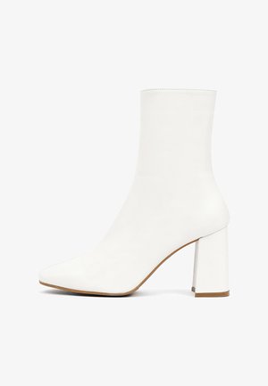 Botte blanche à la cheville en cuir lisse, dotée d'un bout pointu et d'un talon carré épais, avec une texture douce et un design minimaliste.