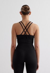 Melnā sporta apģērba komplekts ar siksnu aizmugurē un augsto jostasvietu legingiem, izgatavots no gludas, elastīgas šķiedras.