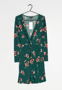 Zelené květované šaty s dlouhými rukávy, zdobené červenými a bílými květinovými vzory, hlubokým výstřihem do V a látkovým páskem v pase.