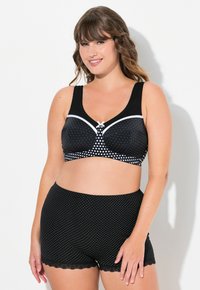 Sostenedor negro con lunares blancos y un lazo en el centro, combinado con pantalones cortos negros a juego con lunares y un dobladillo de encaje.