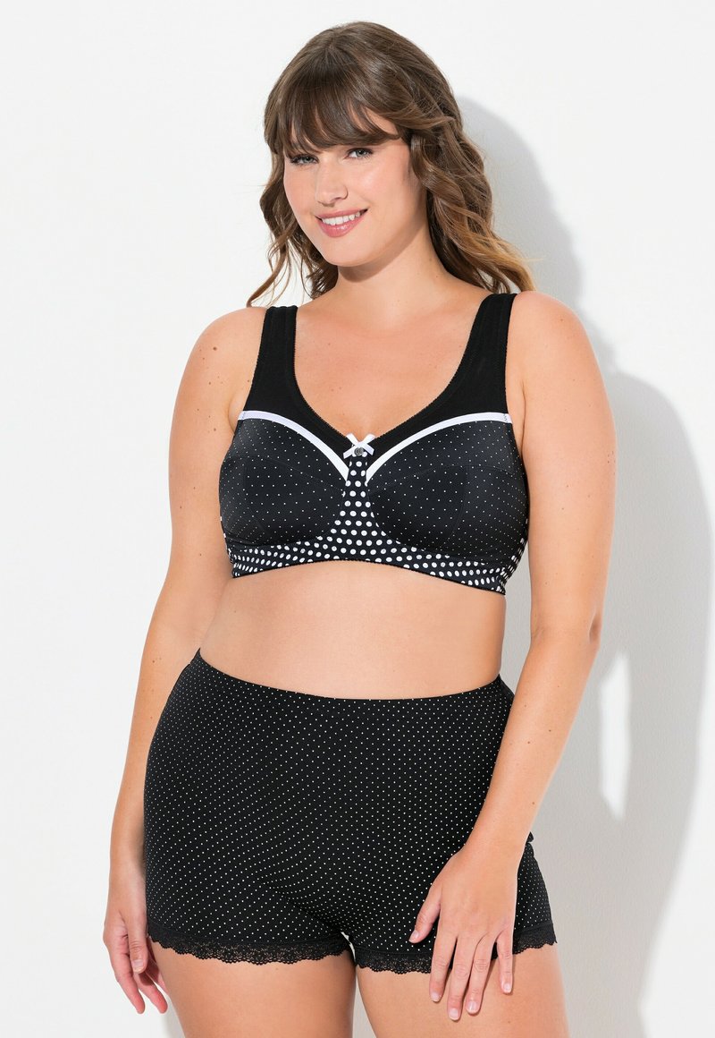 Sostenedor negro con lunares blancos y un lazo en el centro, combinado con pantalones cortos negros a juego con lunares y un dobladillo de encaje.