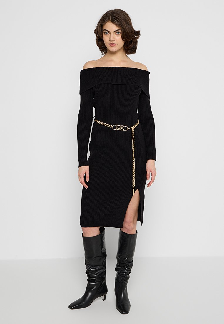 Abito nero a coste con spalline scoperte, maniche lunghe, spacco alto fino alla coscia e cintura in catena dorata. Abbinato a stivali neri alti.