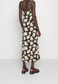 Květinové šaty mají černé pozadí s velkými broskvovými růžemi, tenkými ramínky a volným střihem. Kombinují se s masivními černými sandály.