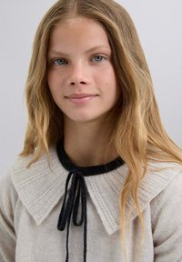 Harmaa villa-neule, jossa on teksturoitu valkoinen kaulus ja mustat yksityiskohdat. Kauluksessa on solmittava suljenta ja rento istuvuus.