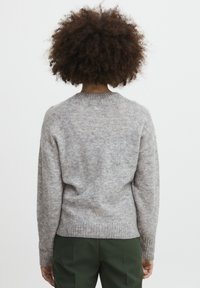 Grå strikket sweater med rund halsudskæring og ribbede manchetter. Blød tekstur og afslappet pasform, parret med grønne bukser. Bagside.