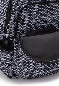 Black and white patterned backpack with a plush monkey keychain, featuring a zippered pocket and a textured fabric surface.