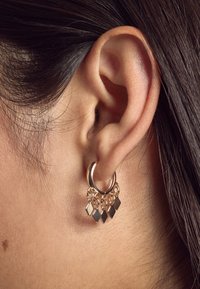 Goldfarbener Creolen-Ohrring mit hängenden, diamantförmigen Akzenten in Schwarz und Gold. Glatte Metalloberfläche; betont das geschichtete Design und den Glanz.