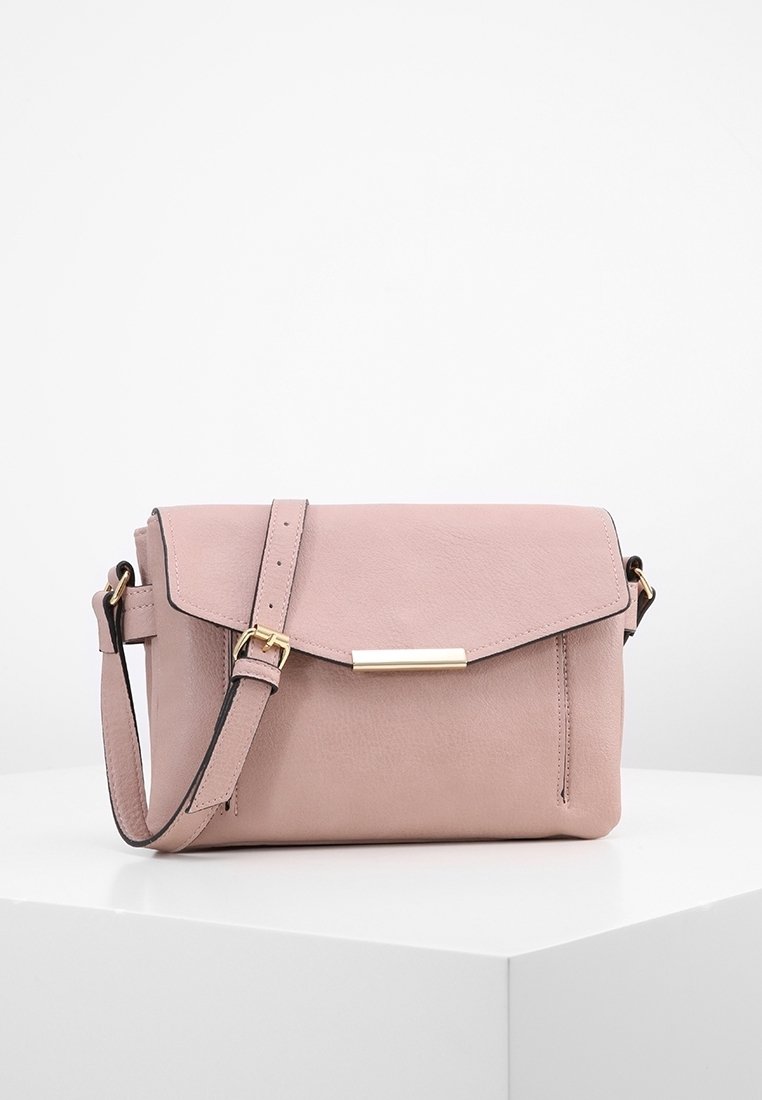Piccola borsa a tracolla morbida di colore rosa con una chiusura rettangolare dorata e una tracolla regolabile, esposta su un podio bianco contro uno sfondo bianco.